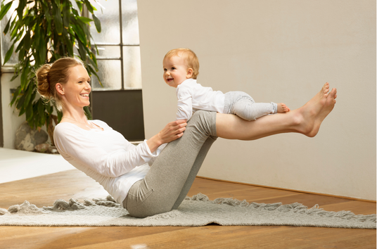 A mother relaxing and working out whilst balancing a baby on her legs